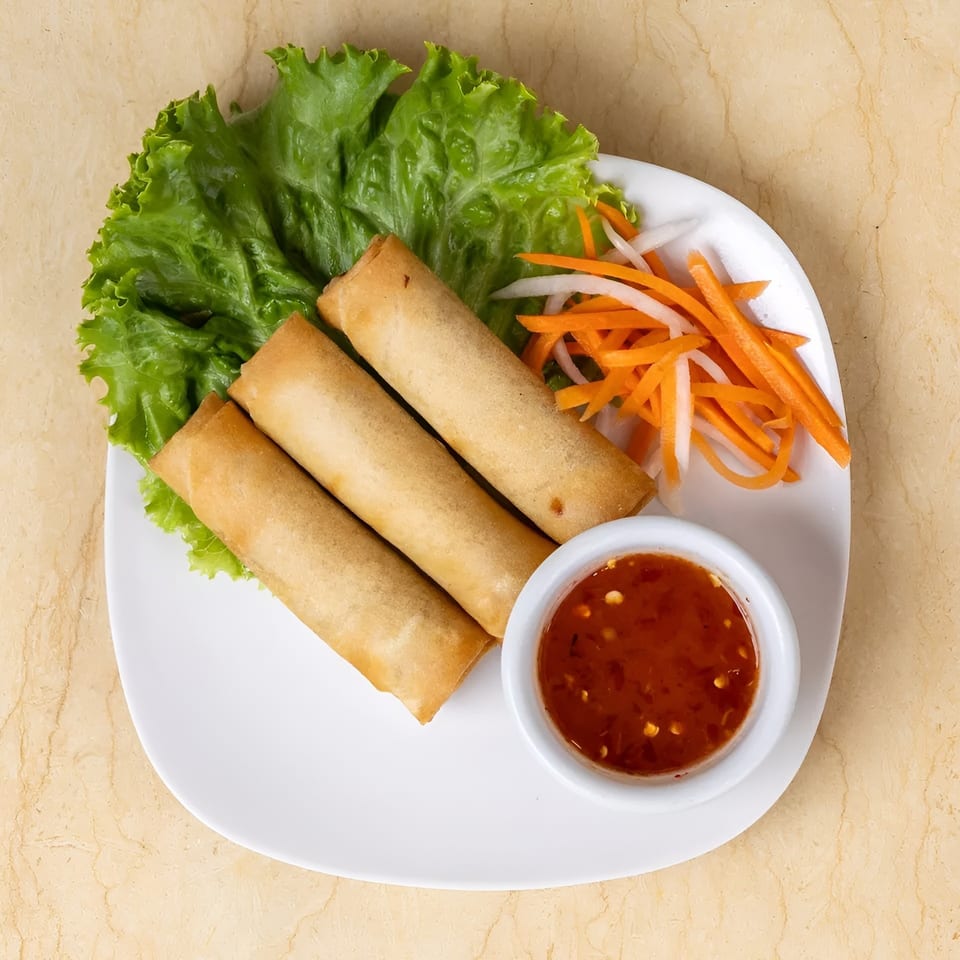 Three golden spring rolls on lettuce with shredded carrots, daikon, and sweet chili sauce.